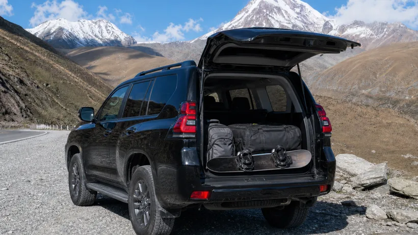 The trunk of an SUV open, showing ample space packed neatly with premium travel bags and a snowboard, highlighting practicality and capacity.